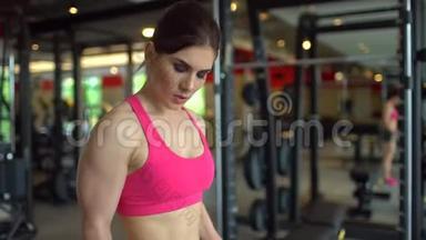 肌肉发达的女运动员穿着粉红色上衣在健身房锻炼举重。 健身女孩在健身房锻炼